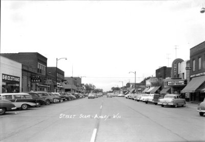 A black and white photo of a street with buildings and cars on either side